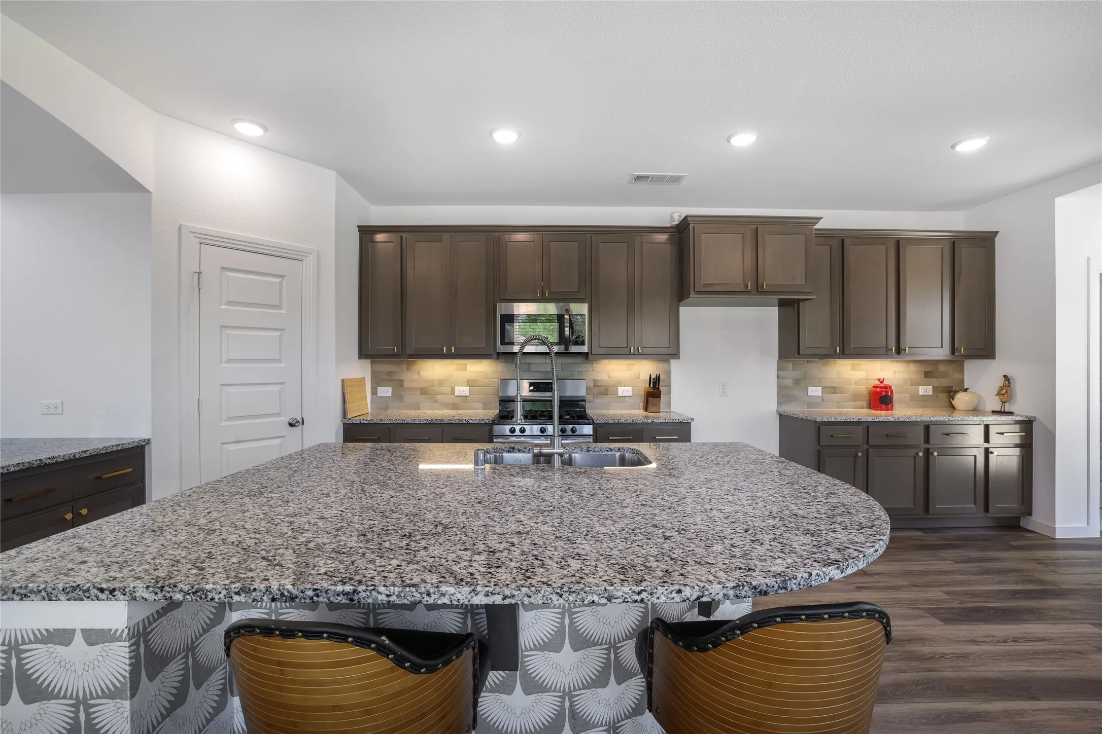 Kitchen featuring dark wood-finish cabinetry, stainless steel appliances, a tile backsplash, recessed lighting, and a spacious island with a stone countertop