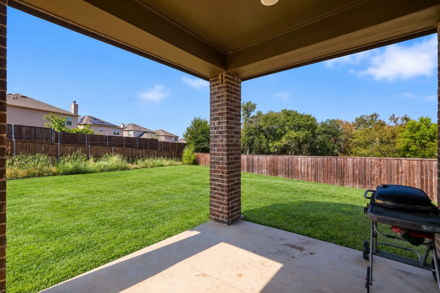 Covered patio with concrete flooring, brick columns, and a spacious lawn