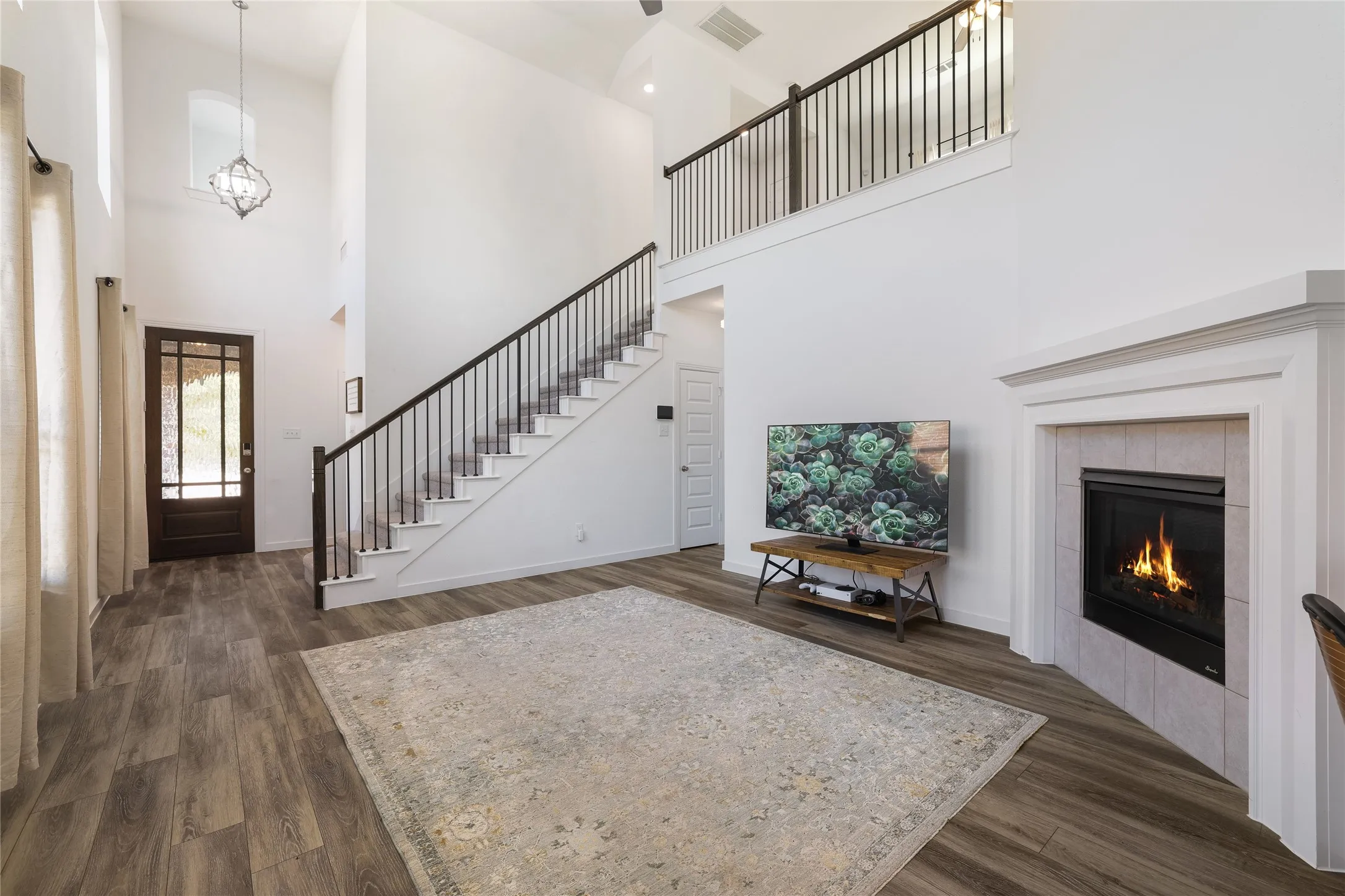Two-story living area featuring a fireplace with a tile surround and mantel, wood-finish flooring, and a staircase with an iron baluster railing