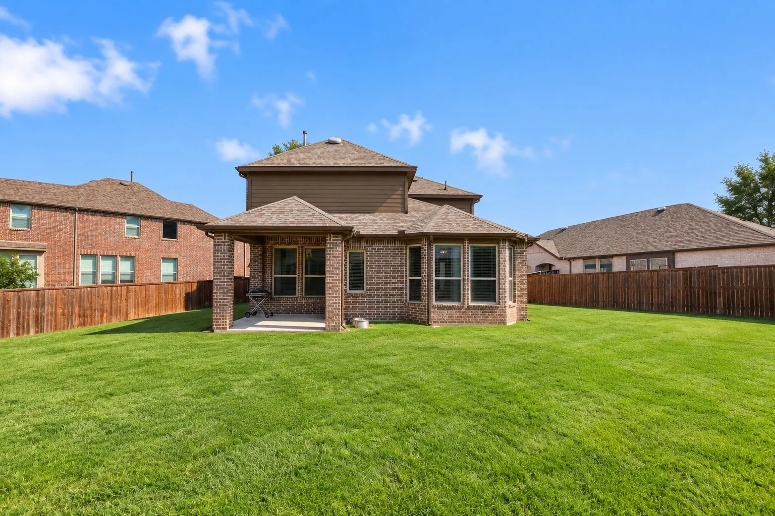 Expansive green lawn with a covered patio featuring a brick facade and multiple windows