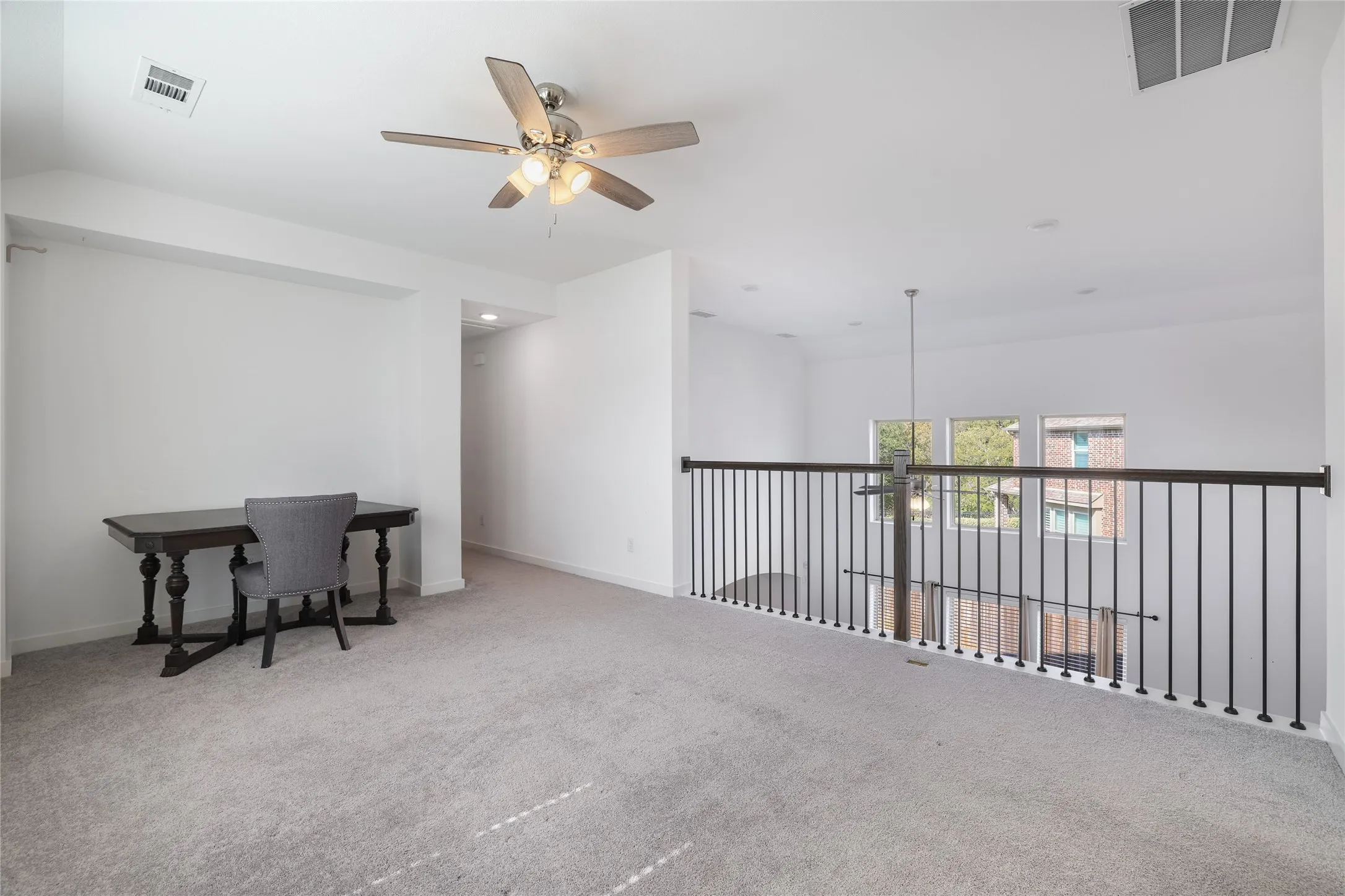 Open loft area featuring carpeting, a ceiling fan with integrated lighting, and a black wrought iron railing