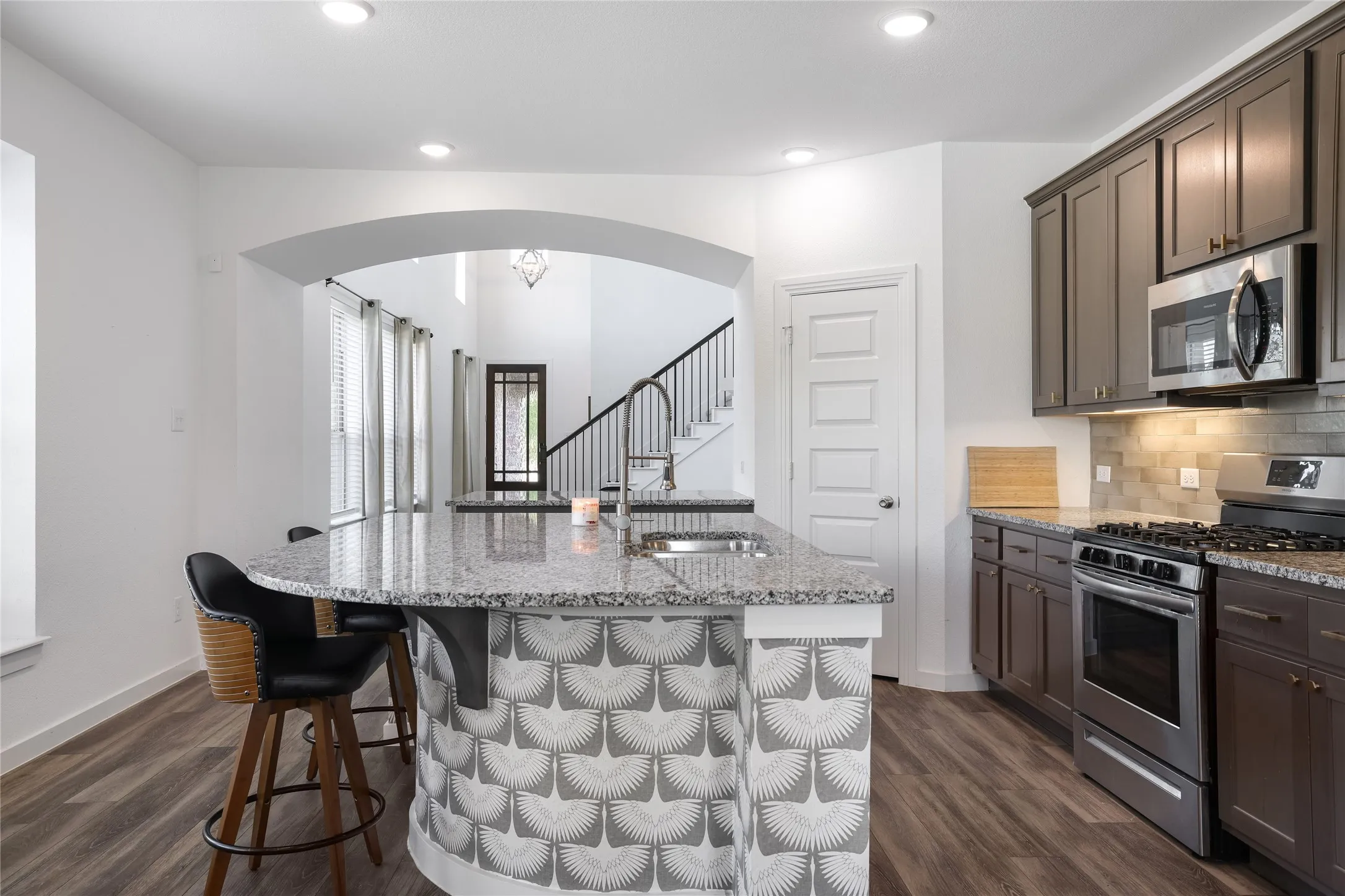 Kitchen featuring dark wood-finish cabinetry, stainless steel appliances, granite countertops, and a tile backsplash