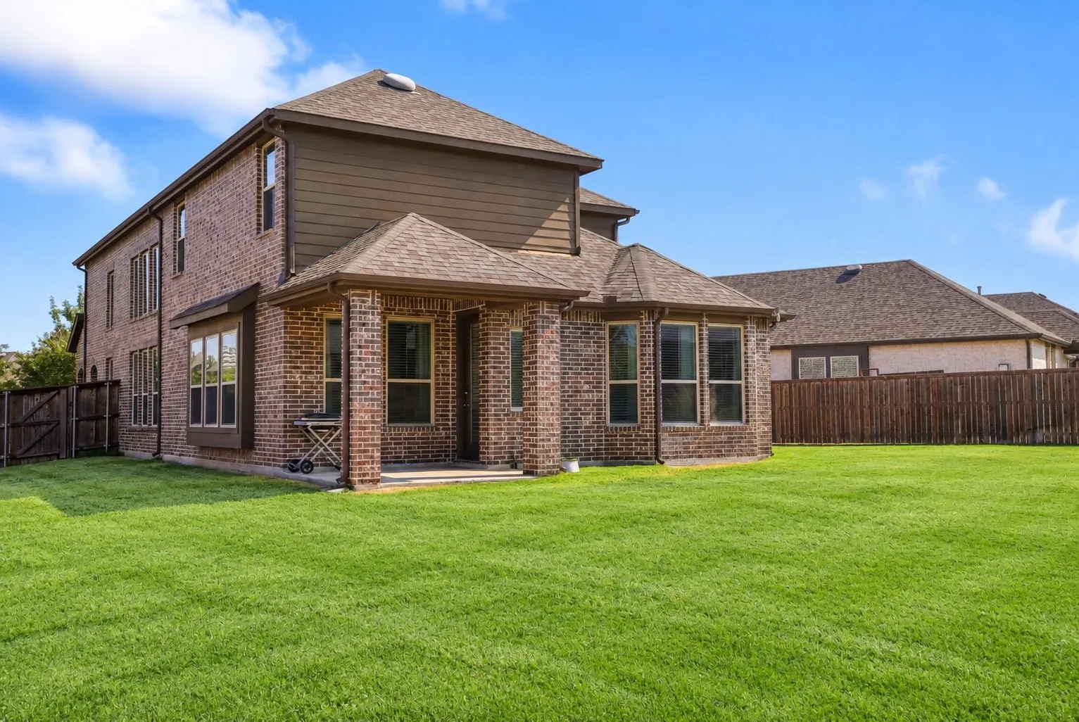 Expansive rear lawn with a brick and siding exterior, multiple windows, and a covered patio area