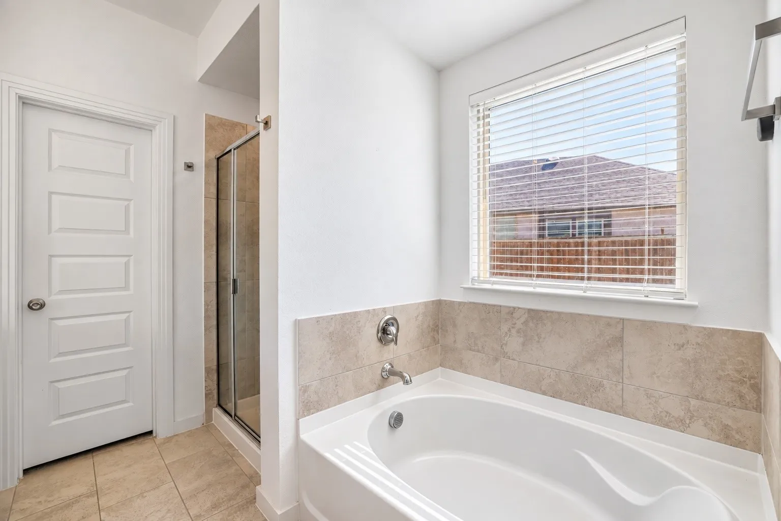 Soaking tub with brushed nickel fixtures, tiled surround, and adjacent glass-enclosed shower