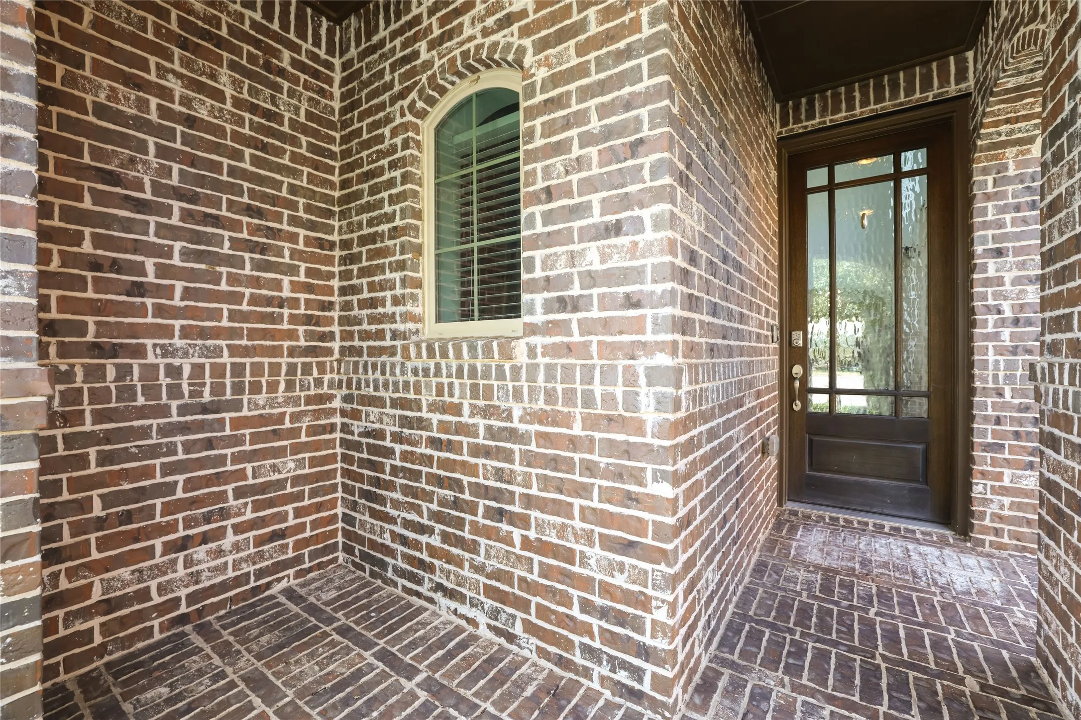 Brick exterior with an arched window, solid wood entry door, and patterned brick flooring