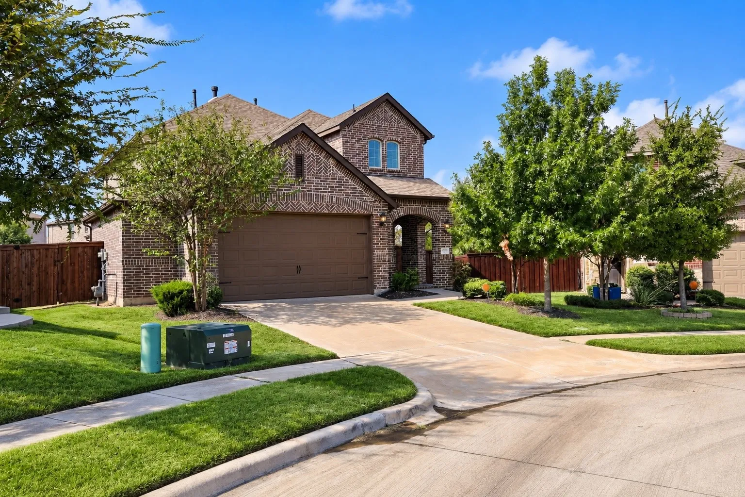 Brick exterior with arched entryway, attached garage, concrete driveway, and mature landscaping