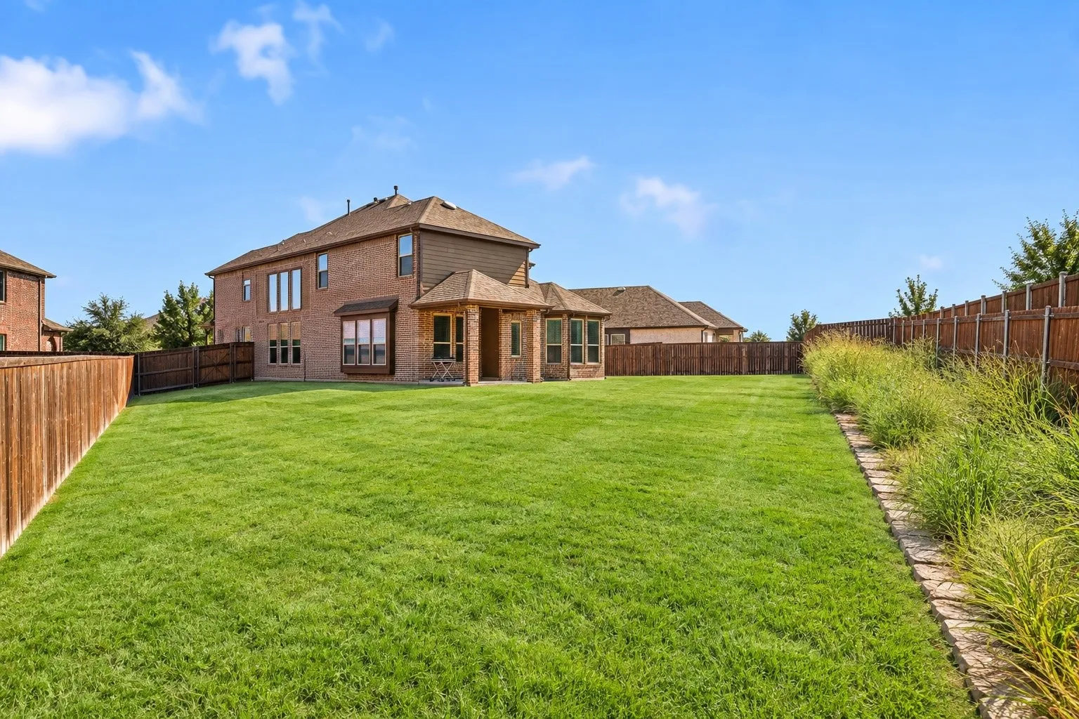 Expansive lawn, brick exterior, multi-paned windows, covered patio, and wood fencing