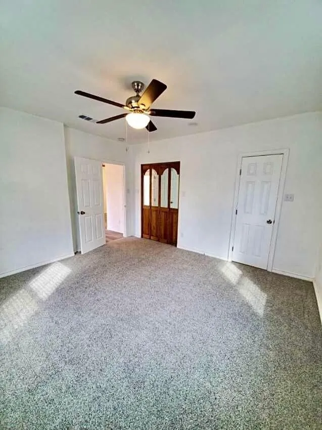 Spacious room featuring neutral carpeting, white walls, a ceiling fan with integrated lighting, and a paneled white door