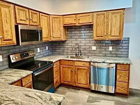 Stainless steel appliances, wood cabinetry, granite countertops, tile backsplash, and a stainless steel sink