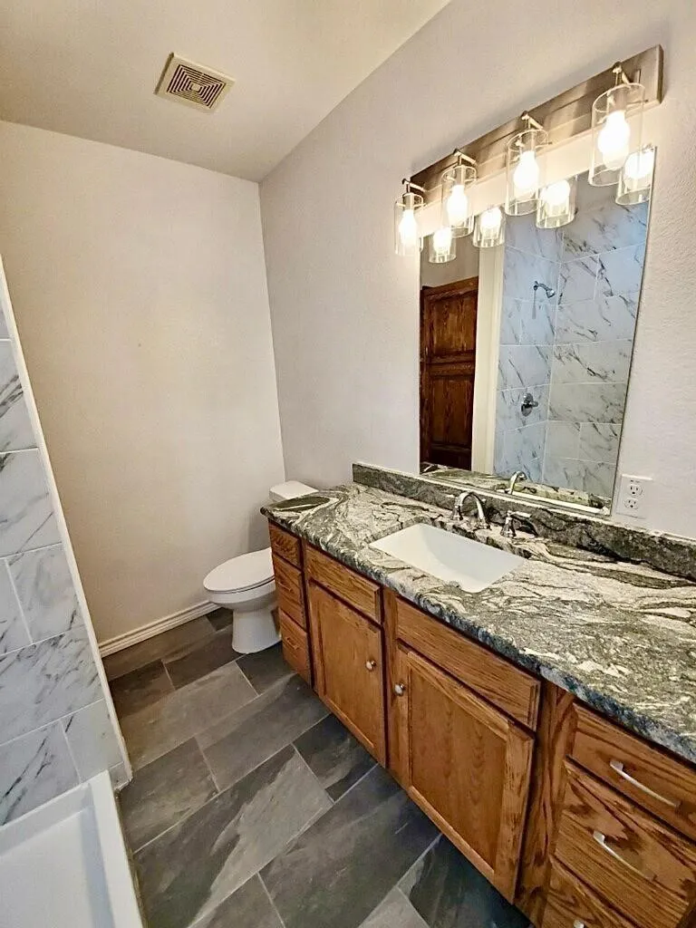 Wood-finish vanity with an integrated sink, stone countertop, and tile flooring