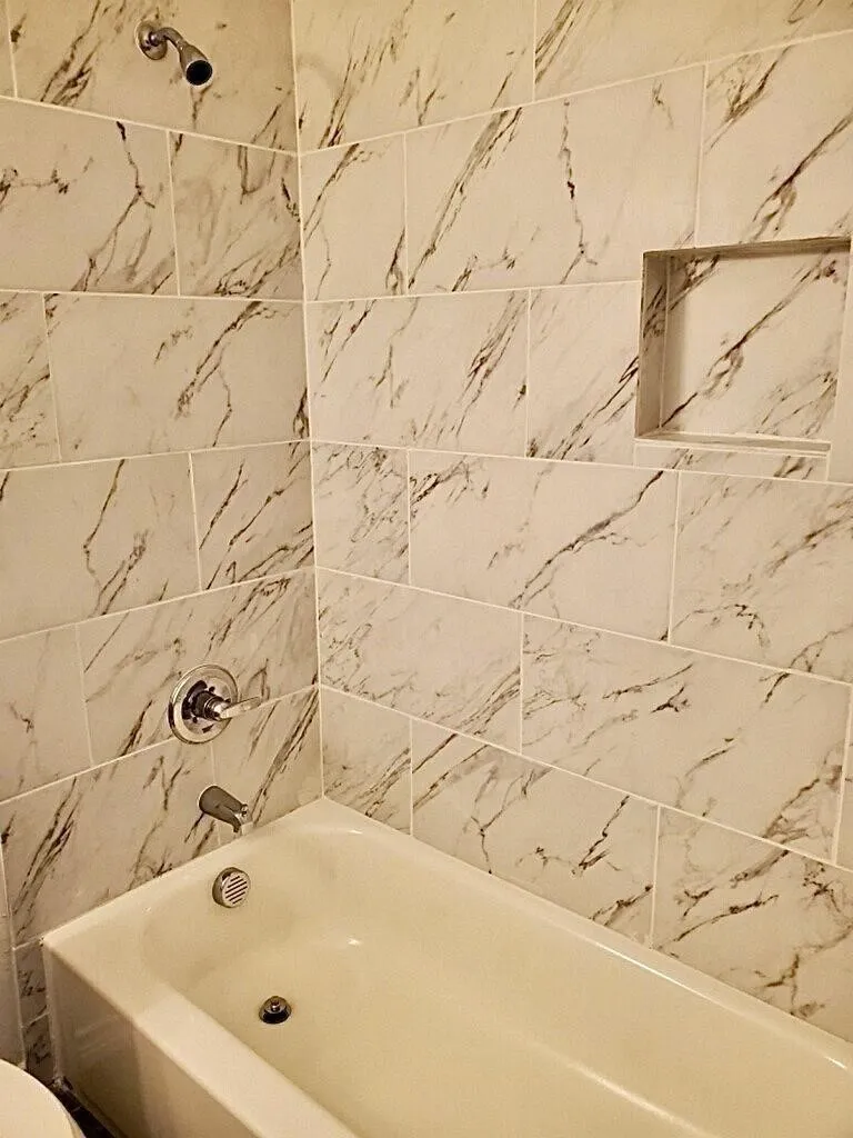 Bathtub with a shower head, polished chrome fixtures, and a tiled surround with an integrated niche