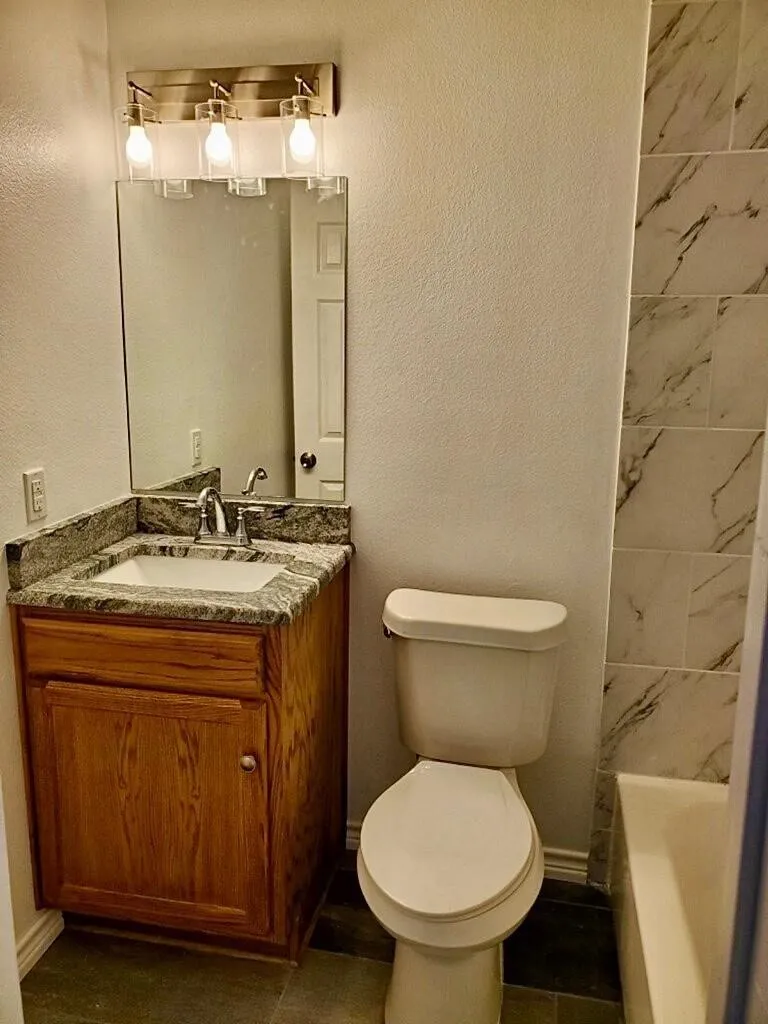 Wood-finish vanity with a granite countertop, undermount sink, and brushed nickel faucet