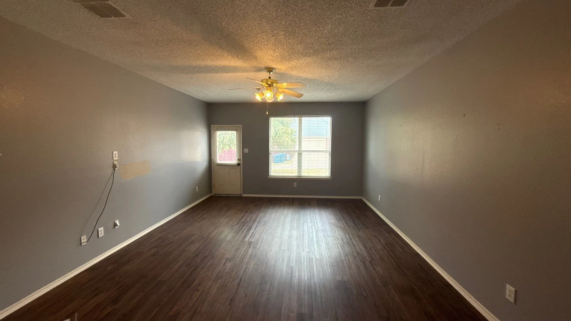 Wood-finish flooring, ceiling fan with integrated lighting, multiple windows, and a rear access door