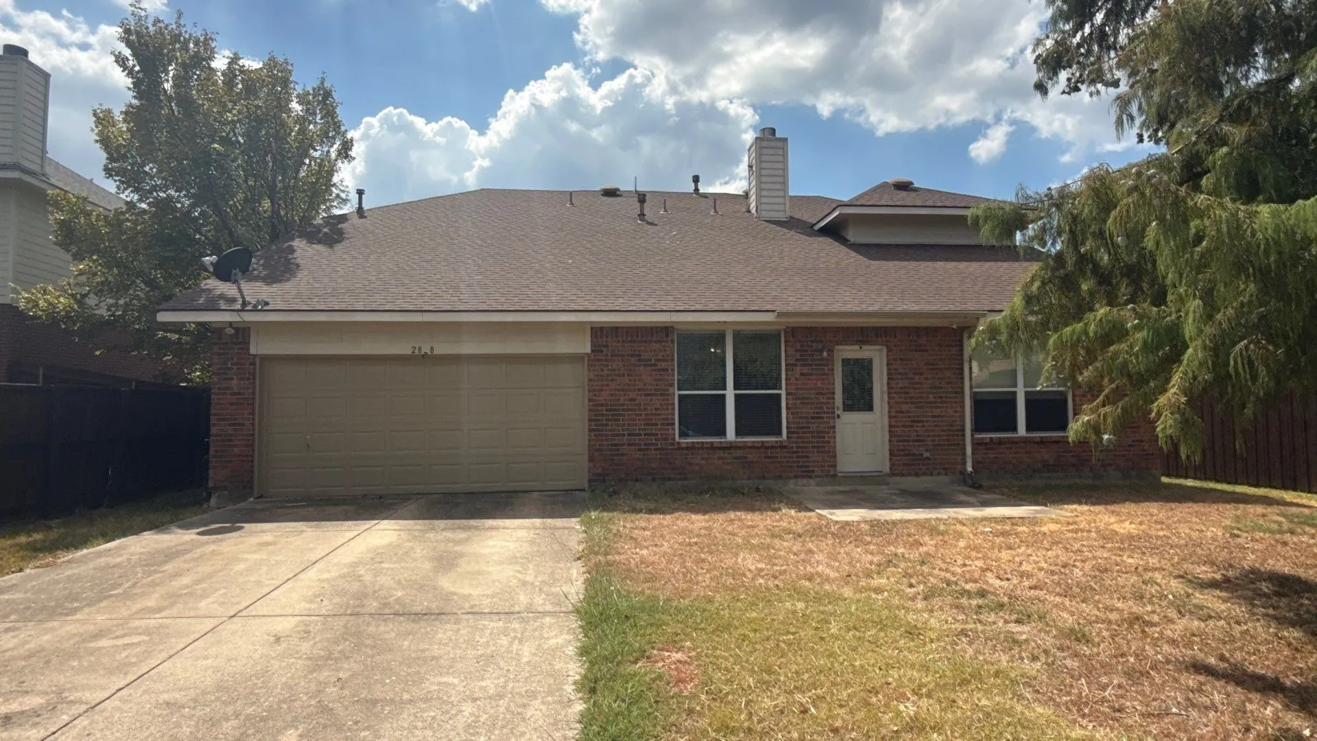 Red brick exterior with a two-car garage, concrete driveway, and a brown shingle roof