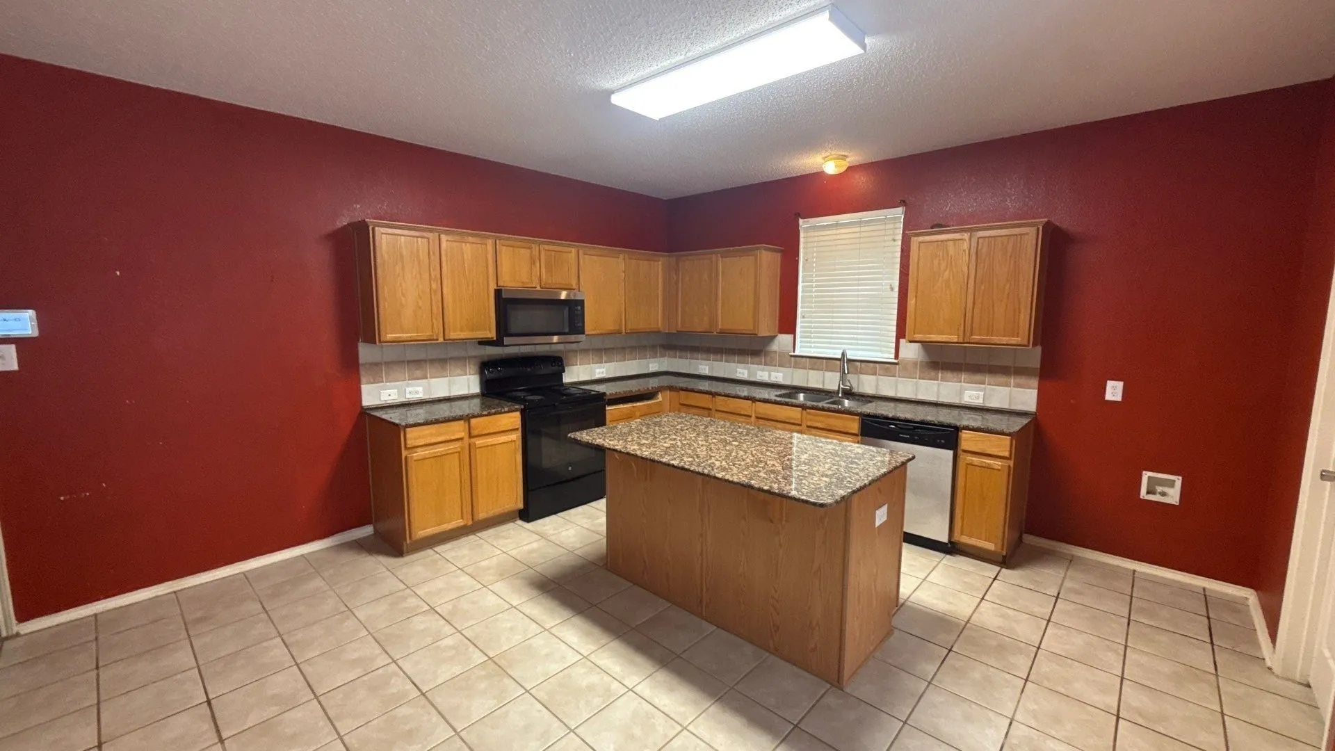U-shaped kitchen with wood-finish cabinetry, a central island, dark granite-style countertops, stainless steel dishwasher, and tile flooring