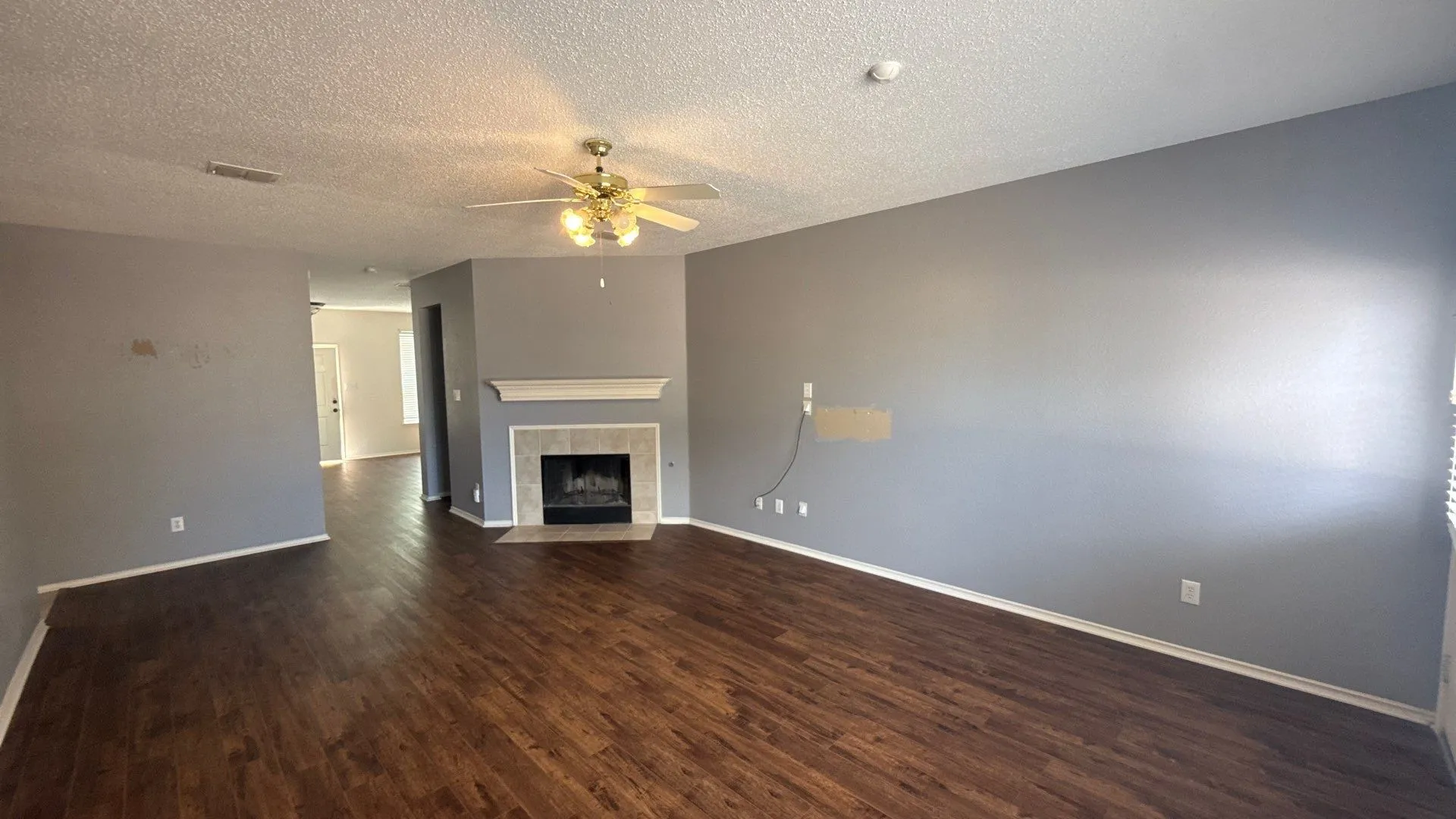 Wood-finish flooring throughout, ceiling fan with integrated lighting, and a corner fireplace with a mantel and tile surround