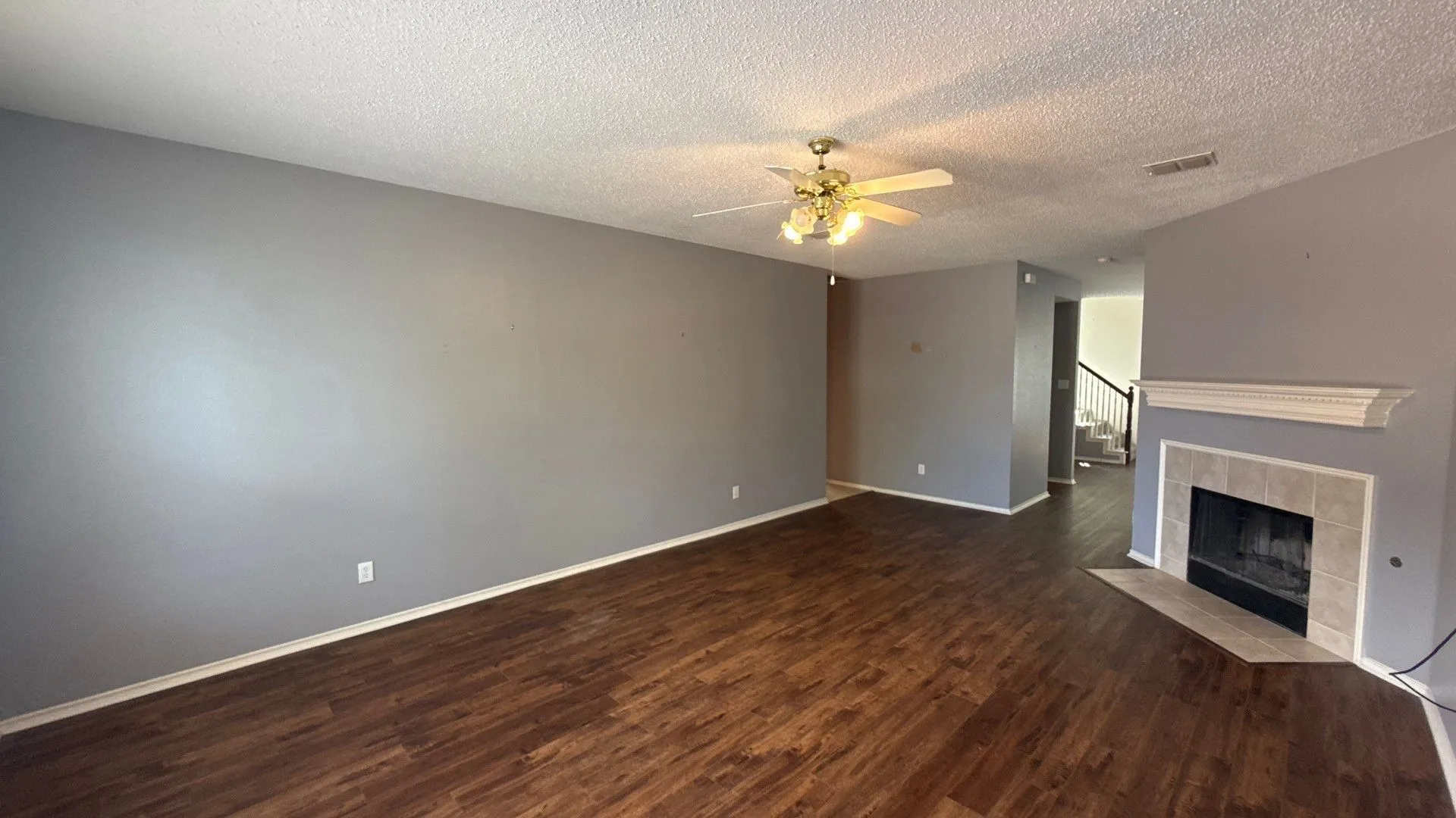 Spacious living area featuring wood-finish flooring, a ceiling fan with integrated lighting, and a fireplace with a tile surround and mantel
