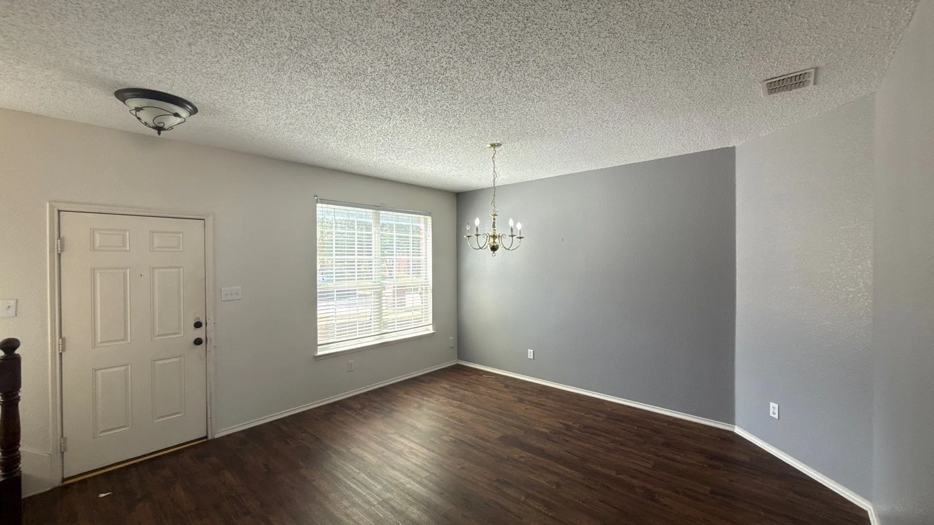 Wood-finish flooring with baseboards, a multi-pane window with blinds, and a brass chandelier