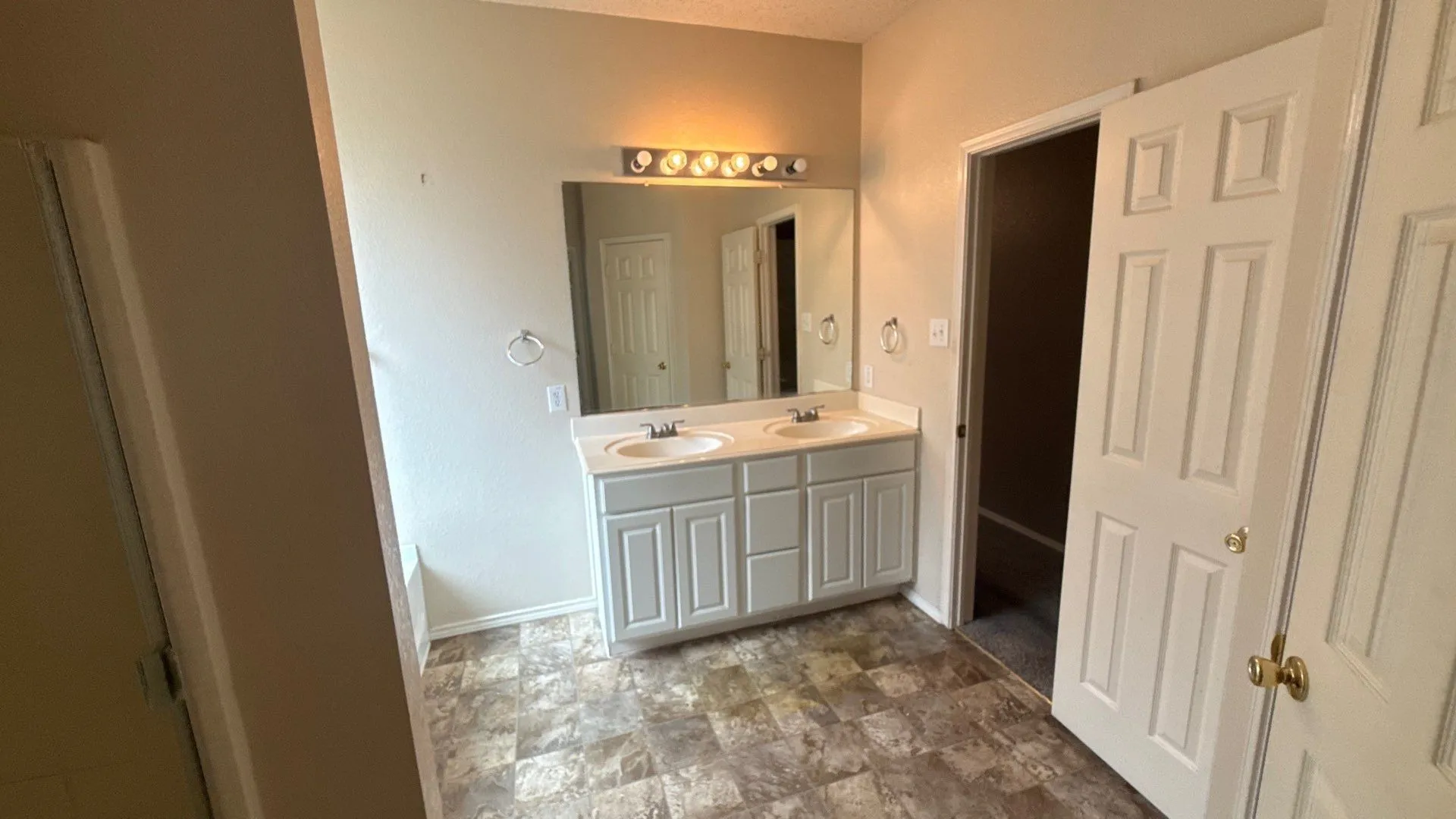 Dual vanity with undermount sinks and light-toned countertop, large wall-mounted mirror, and tile-pattern flooring