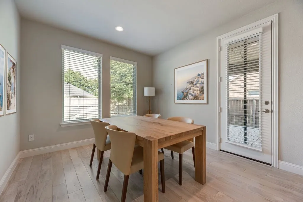 Wood-finish flooring with light-toned walls, two windows with blinds, a recessed ceiling light, and a white door with integrated blinds