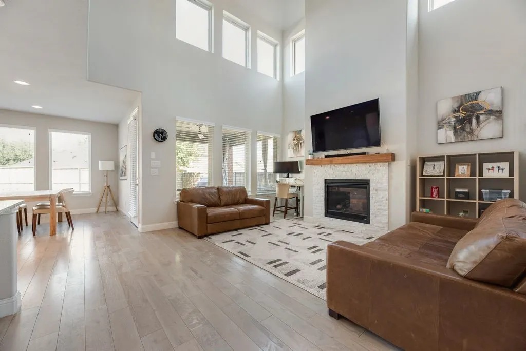 Two-story living area with high ceilings, wood-finish flooring, a stone-clad fireplace with a wood mantel, and multiple large windows