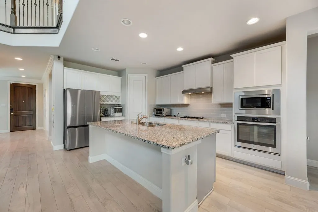 Kitchen featuring a center island with a granite countertop, stainless steel appliances, white cabinetry, and wood-finish flooring