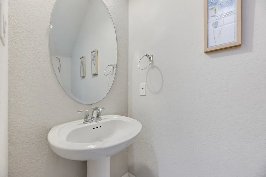 Pedestal sink with a chrome faucet, complemented by an oval wall-mounted mirror