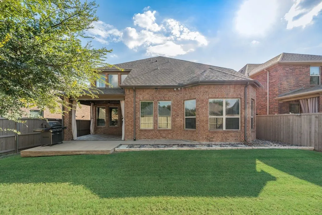 Brick exterior with an expansive lawn, covered patio, and wood privacy fencing