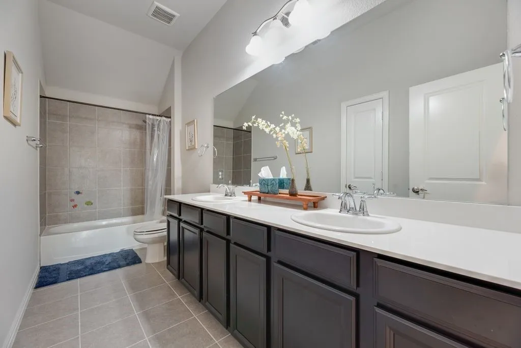 Dual basin vanity with dark wood-finish cabinetry, a large integrated mirror, and chrome fixtures