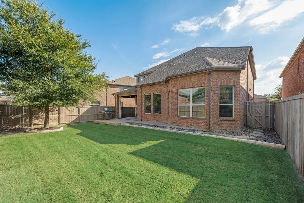 Expansive grassy yard with a wooden privacy fence, mature tree, and a covered patio