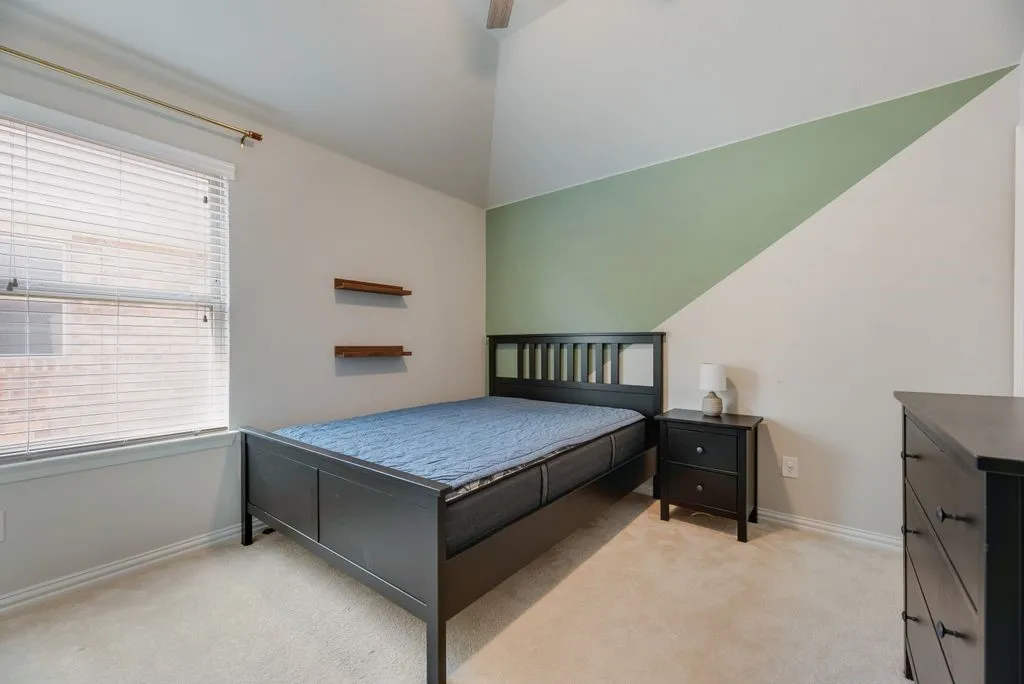 Vaulted ceiling with angled accent wall, carpeted flooring, and window with blinds