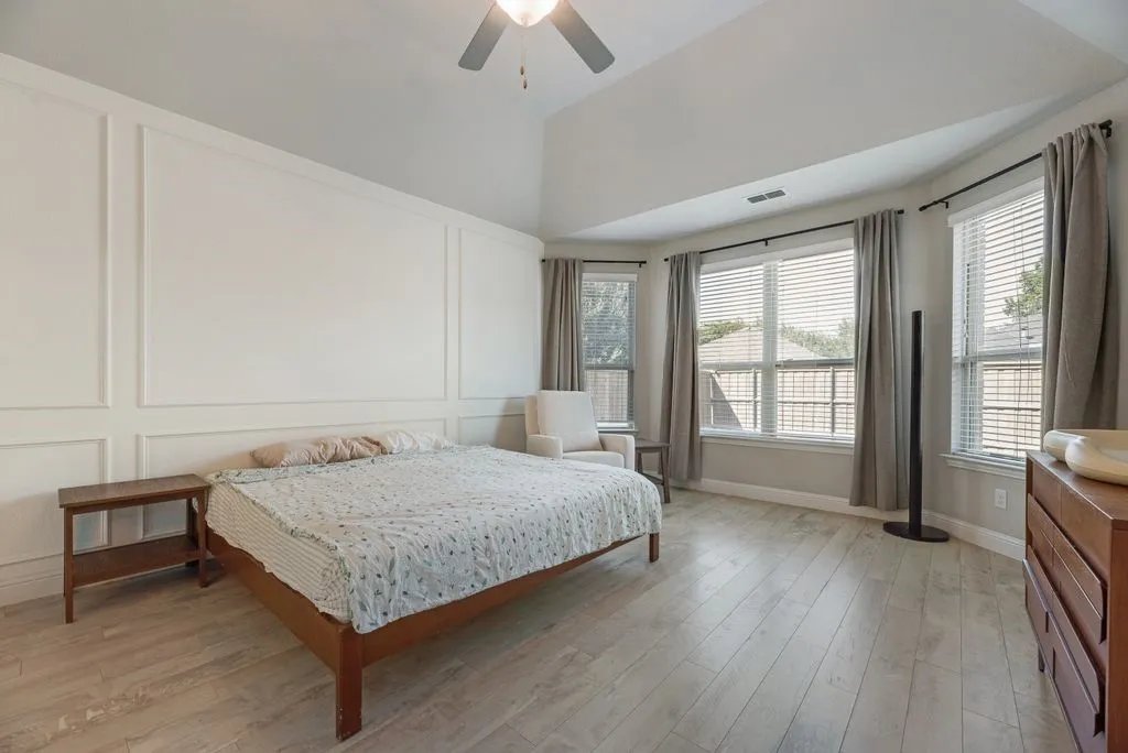 Vaulted ceiling with a ceiling fan, accent wall with decorative molding, wood-finish flooring, and multiple windows with blinds