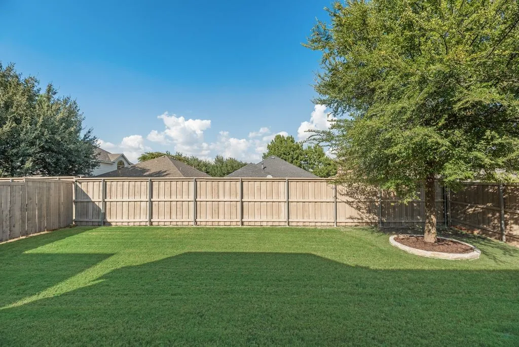 Expansive backyard featuring a manicured lawn, established tree, and wood privacy fencing