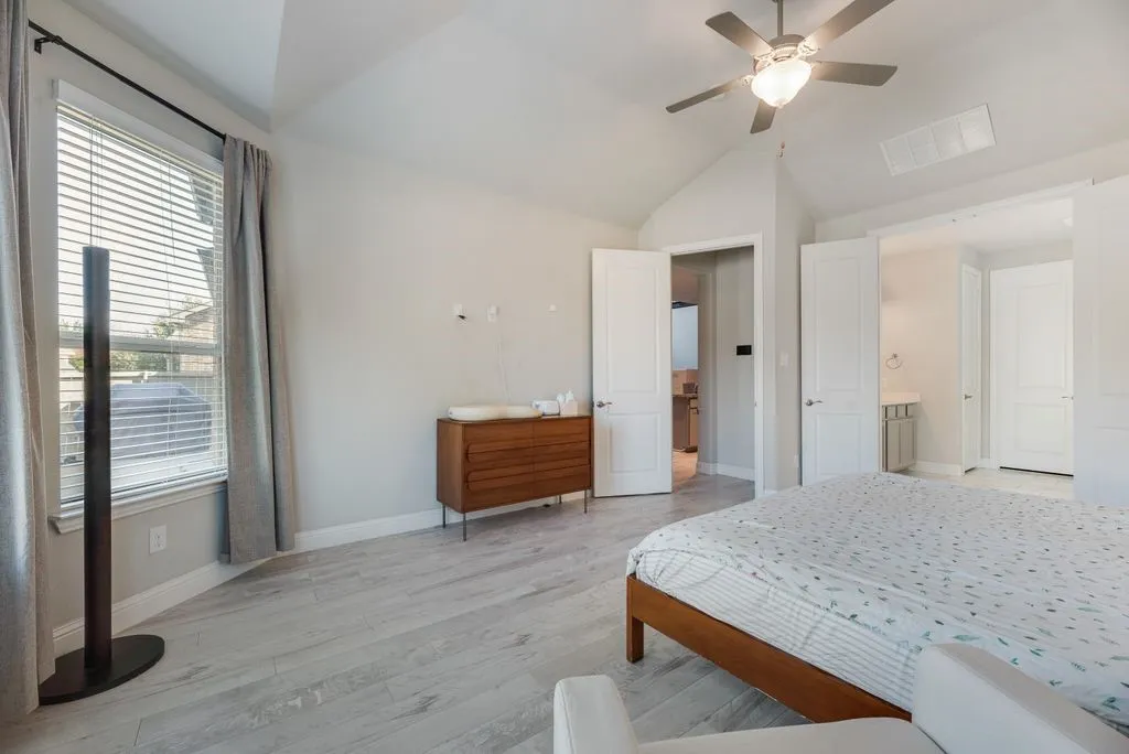 Vaulted ceiling with a ceiling fan, light wood-finish flooring, and multiple doorways