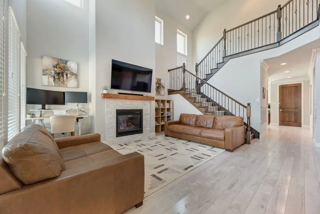 Two-story living area with high ceilings, light wood-finish flooring, and a fireplace with a white tile surround