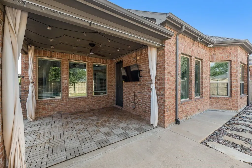 Covered patio featuring wood-finish tile flooring, a ceiling fan, string lighting, and attached privacy curtains
