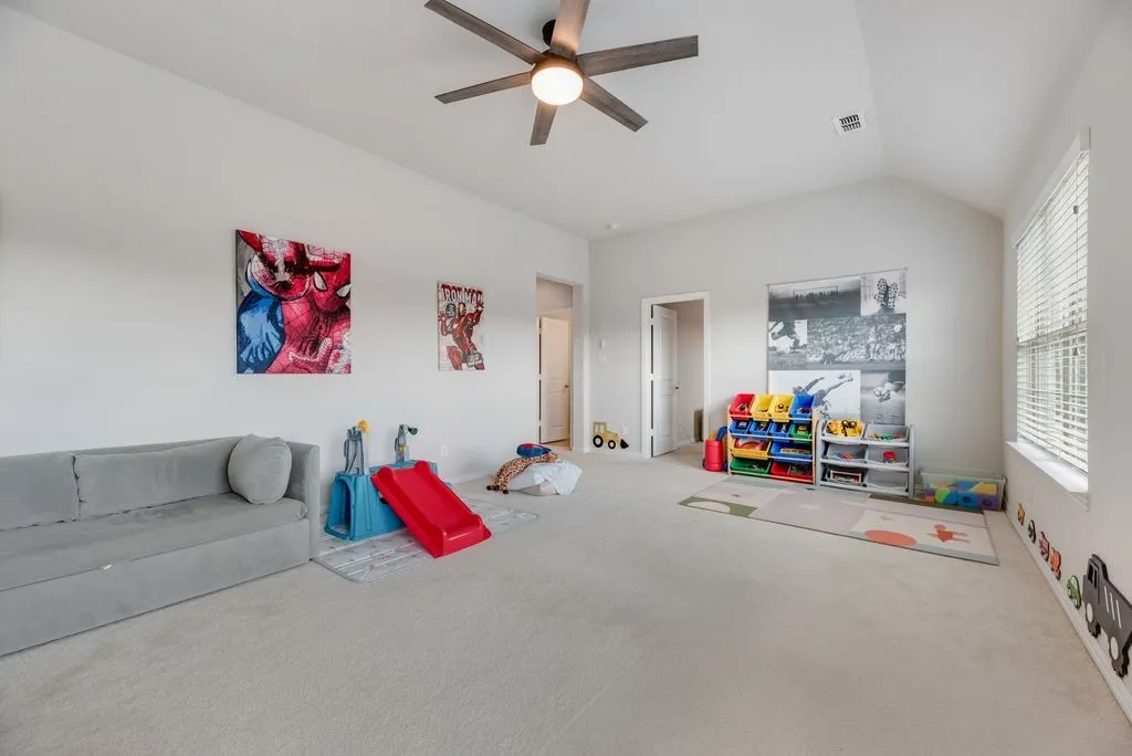 Vaulted ceilings, neutral carpet flooring, ceiling fan with light fixture, and a window with blinds