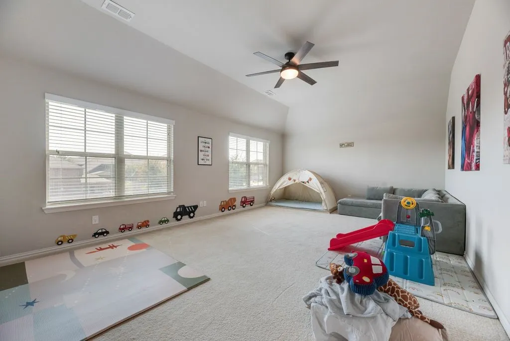 Vaulted ceiling, ceiling fan, two windows with blinds, and light-colored carpeting