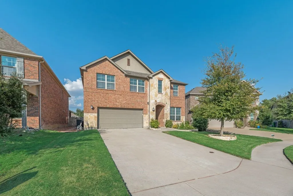 Two-story exterior with brick and stone accents, an attached garage, a concrete driveway, and a manicured lawn