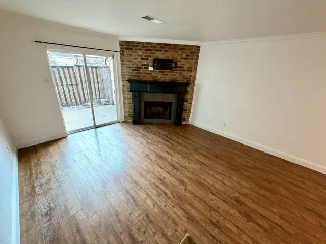 Wood-finish flooring, brick-faced fireplace, dark wood-tone mantel, and sliding glass patio door