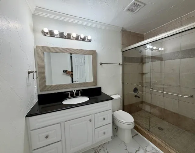 Vanity with a black countertop and integrated sink, framed mirror, and a walk-in shower with clear glass enclosure and tiled walls