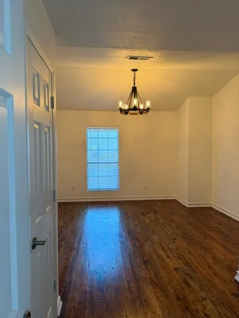 Wood-finish flooring, single window with horizontal blinds, overhead chandelier, and white paneled door