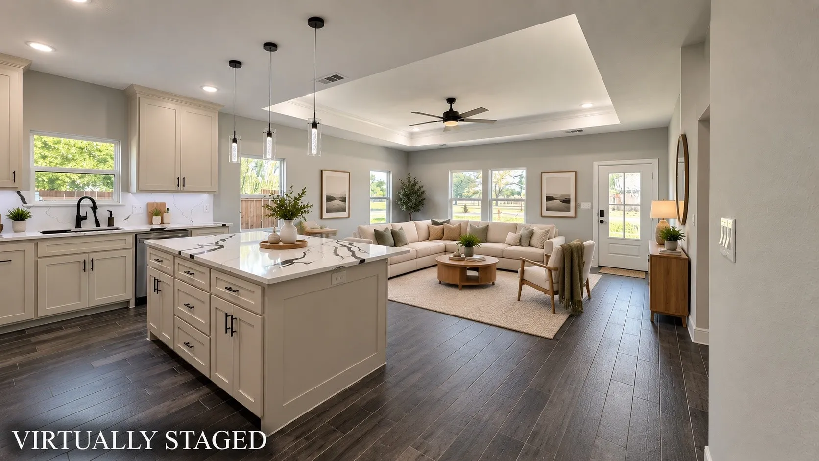 Expansive open-concept living area featuring wood-finish flooring, a kitchen island with stone countertop, recessed lighting, and a tray ceiling