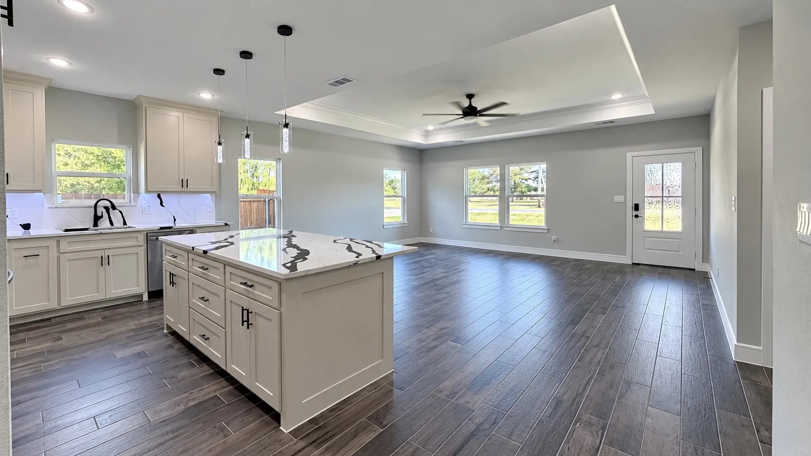 Spacious interior featuring wood-finish flooring, a kitchen island with a patterned countertop, recessed lighting, and a ceiling fan