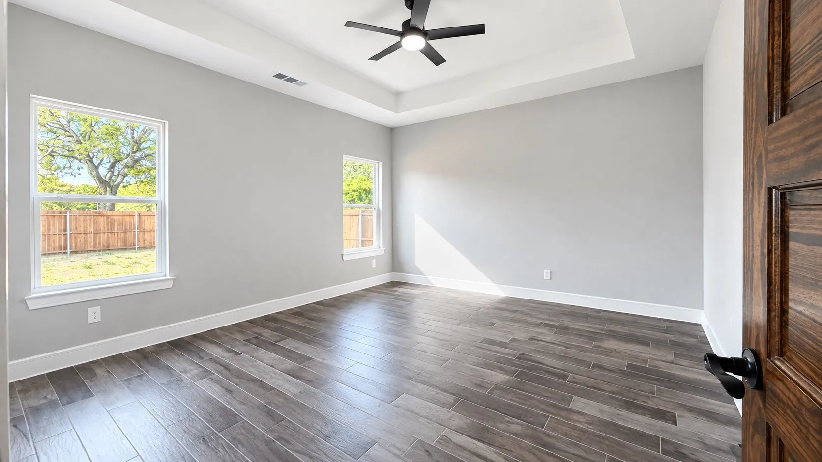 Tray ceiling with a ceiling fan, wood-finish flooring, and natural light from multiple windows