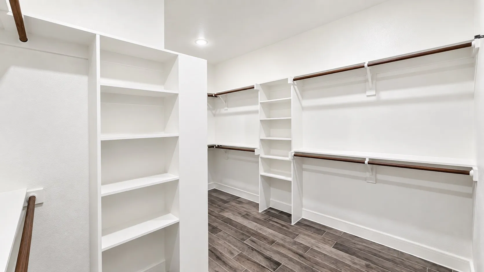 Custom closet system featuring built-in shelving, multiple hanging rods, and wood-finish flooring