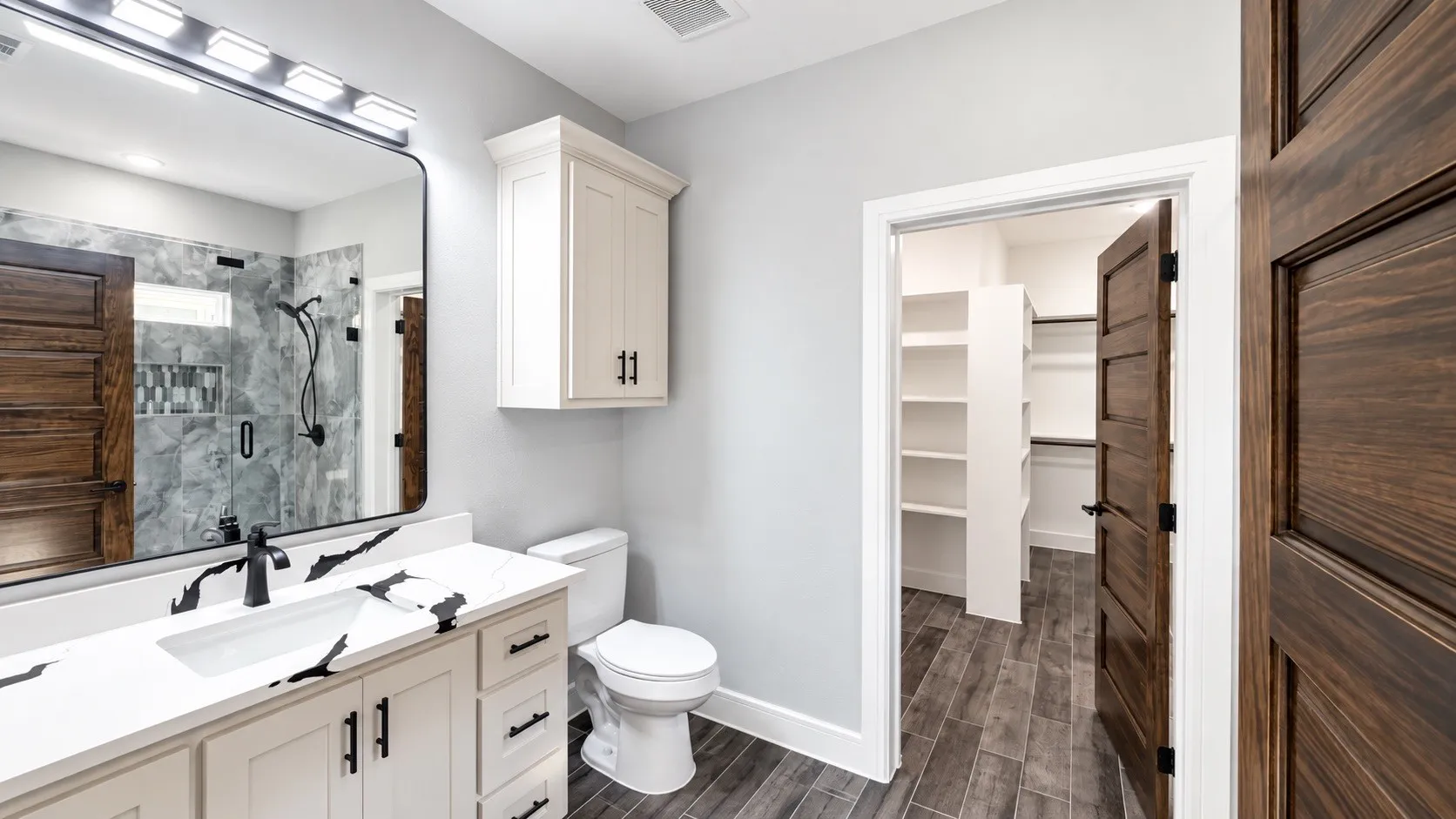 Vanity with integrated sink and quartz-finish countertop, white cabinetry with matte black hardware, wood-look flooring, and a walk-in closet with shelving