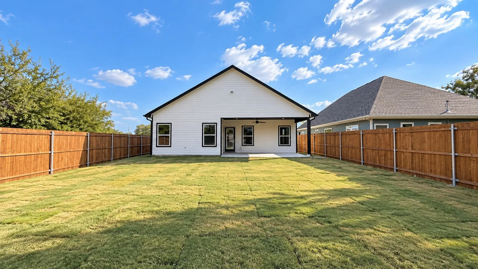 Expansive backyard featuring a manicured lawn, wood privacy fencing, and a covered concrete patio