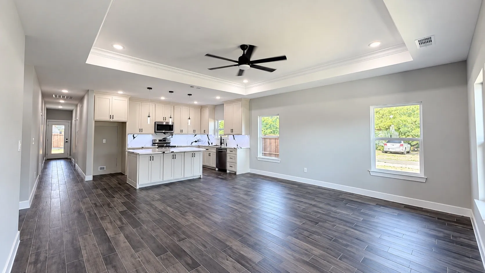 Open-concept living area with wood-finish flooring, a tray ceiling, and recessed lighting