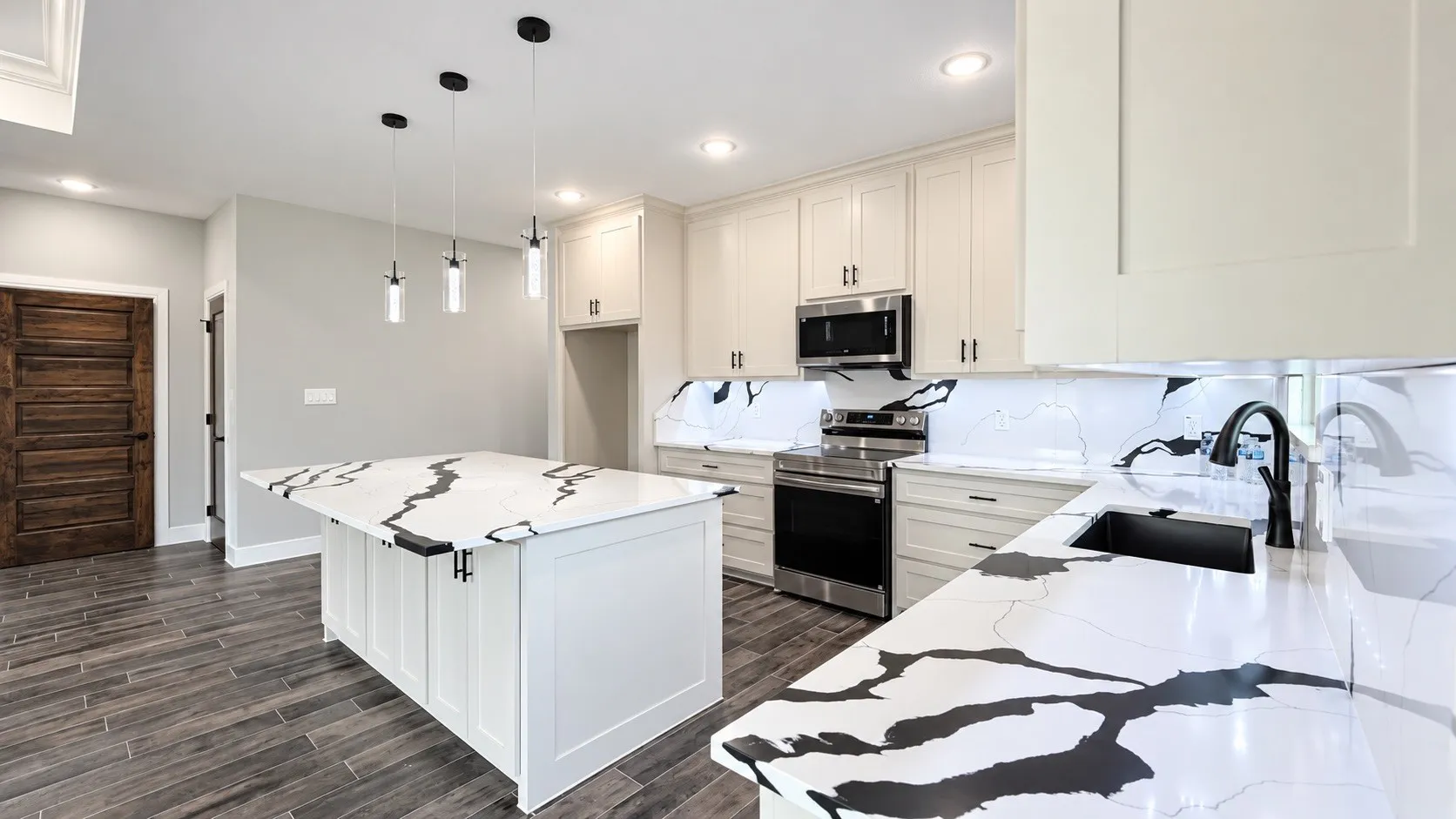 White cabinetry with black hardware, stainless steel appliances, striking white countertops with black veining, an undermount sink with a matte black faucet, and wood-finish flooring